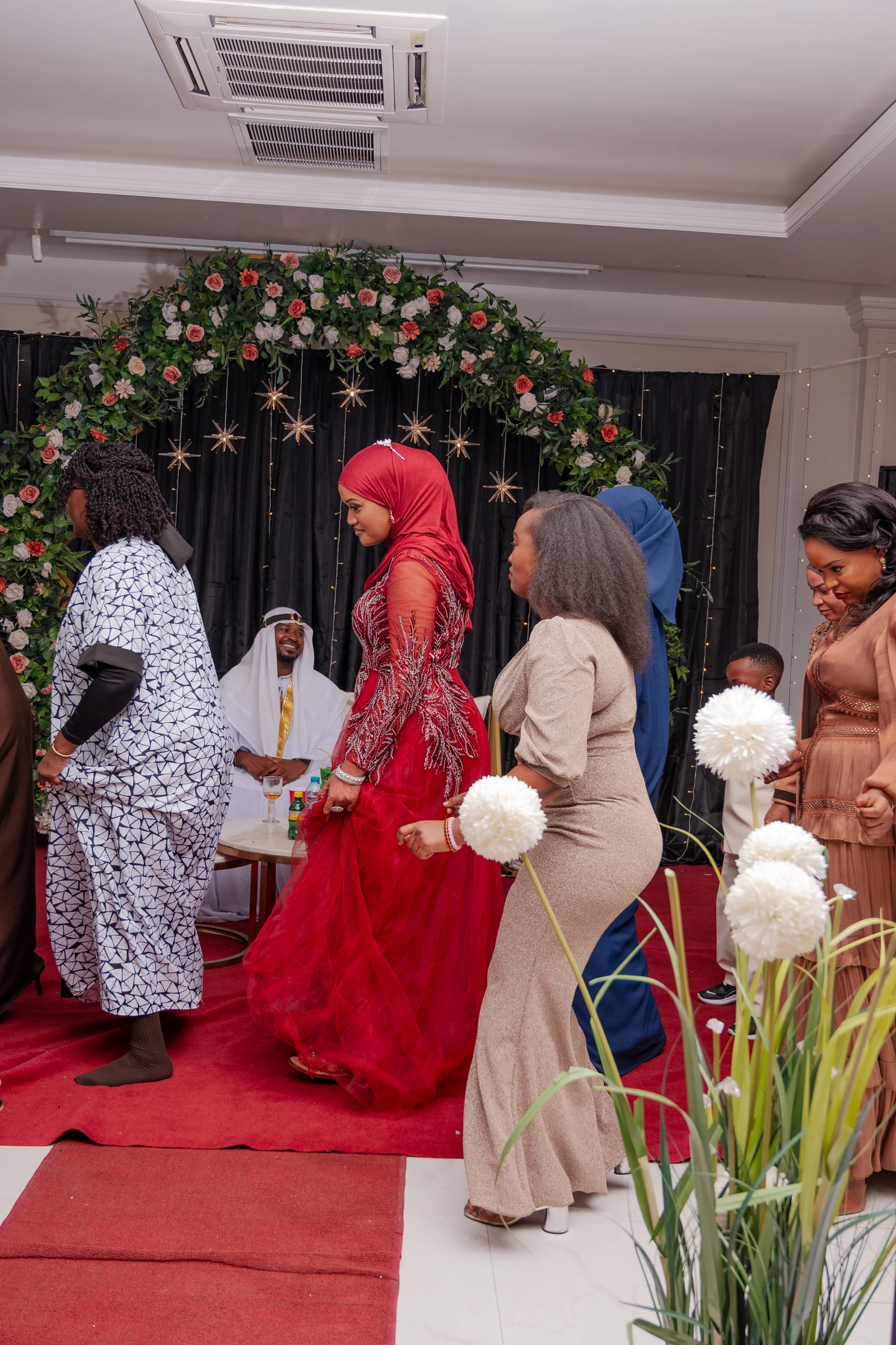 Wedding participants beside a floral backdrop and red carpet